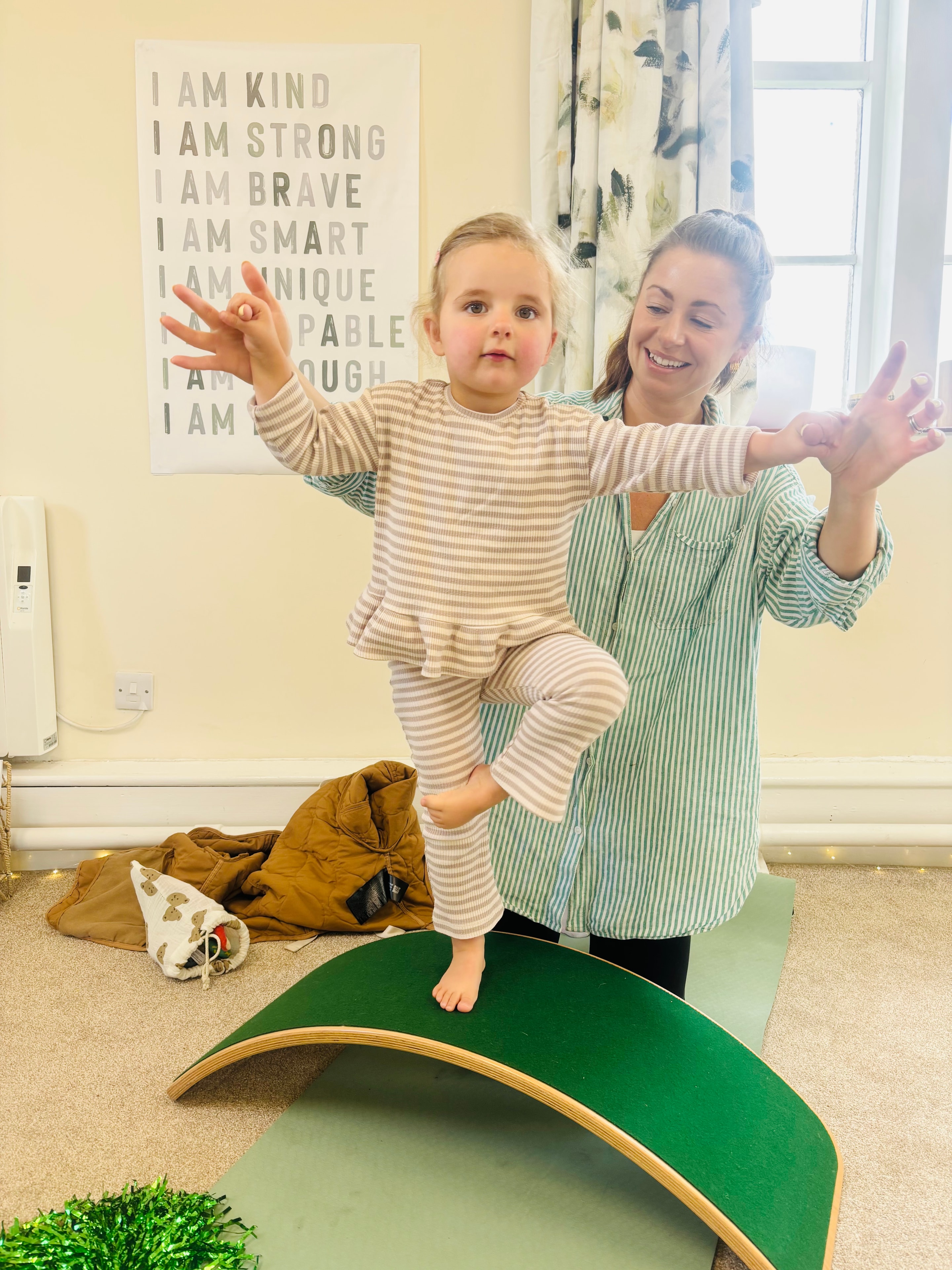 Georgie helping a toddler balance on a Wobbel board at Buddha Bears